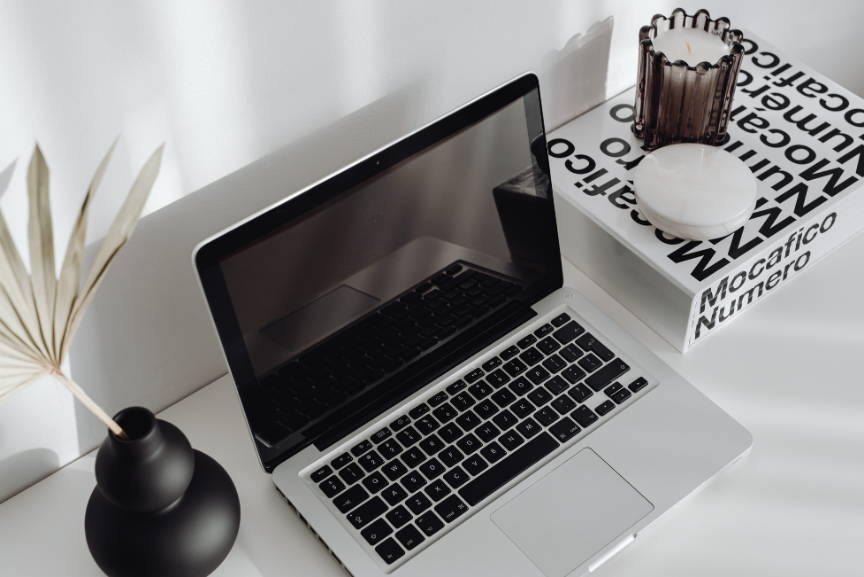 Laptop on desk with black and white book to side and candle